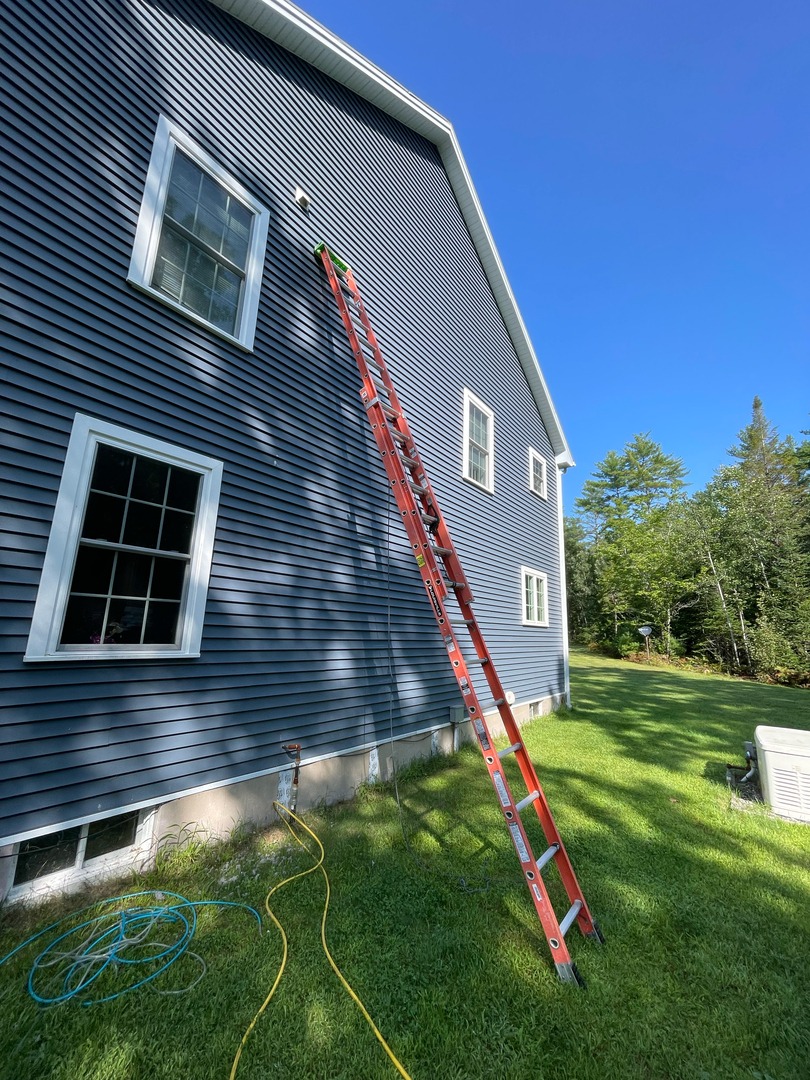 Residential exterior maintenance at a two-story home in Maine, featuring an extension ladder positioned against the siding near an upper-level vent. Upfront Home Inspection & Maintenance provides professional home inspections and preventative maintenance services throughout Southern and Central Maine.