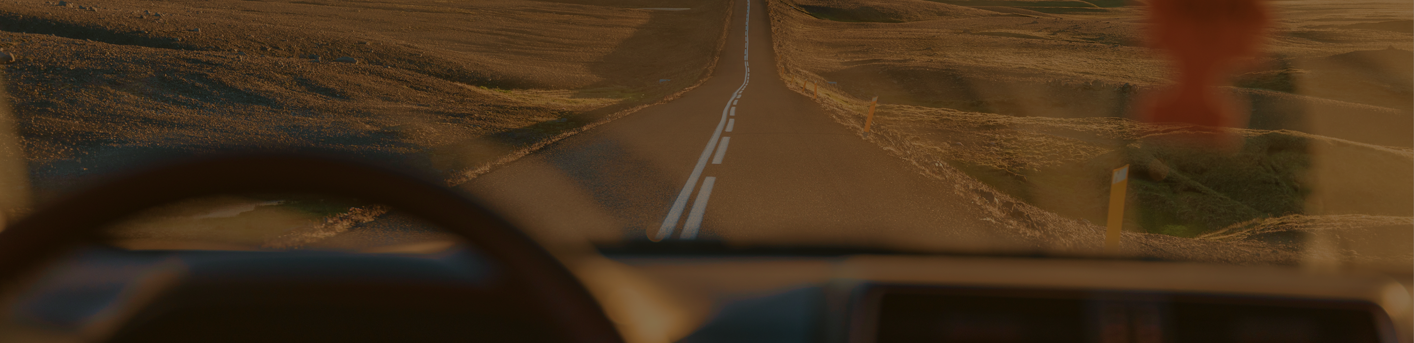 View from the inside of a car windshield looking out towards a road cutting through fields.