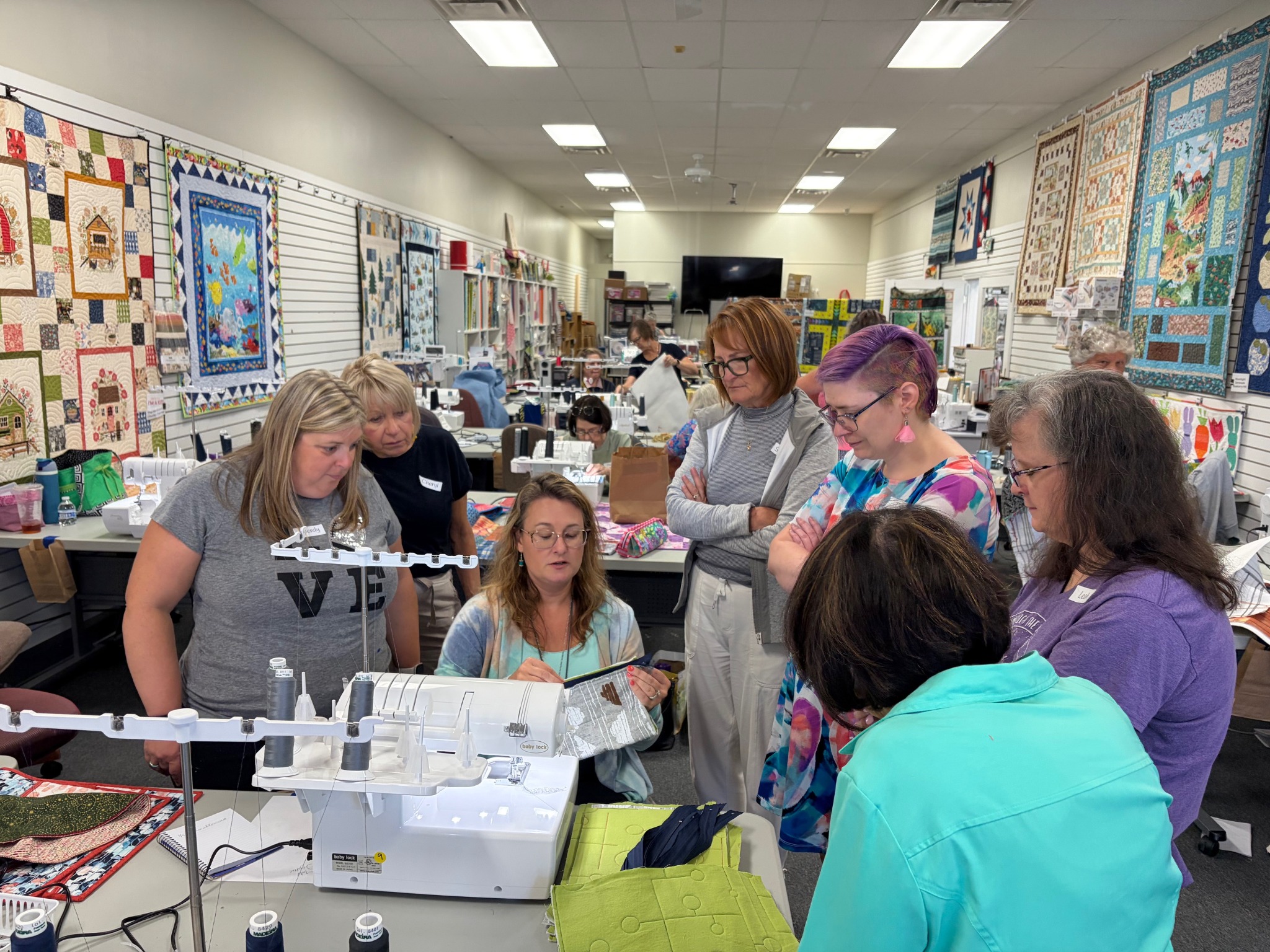 Students gather around for a live Decorative Stitch demonstration, learning serger and decorative stitching techniques in a hands-on quilting workshop designed to inspire creativity and confidence.