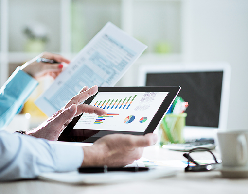 Two people looking at charts on a tablet and information in a printed document.