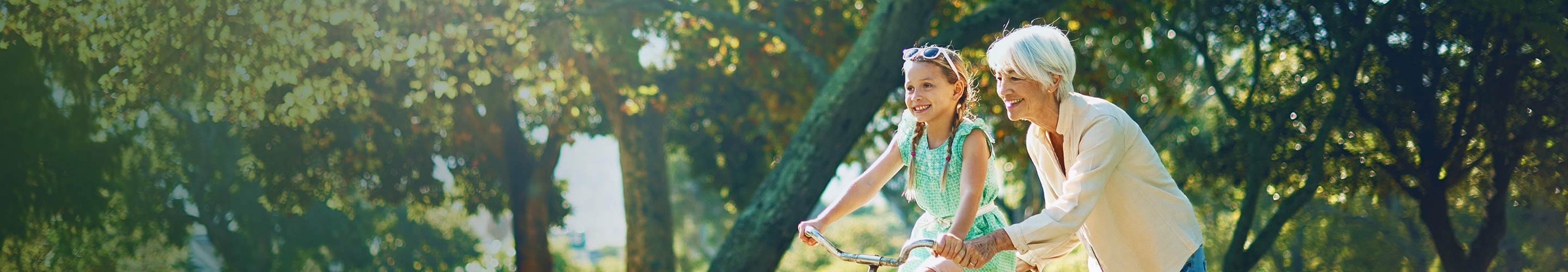 A grandmother teaching her young granddaughter to ride a bike in the park on a sunny day.