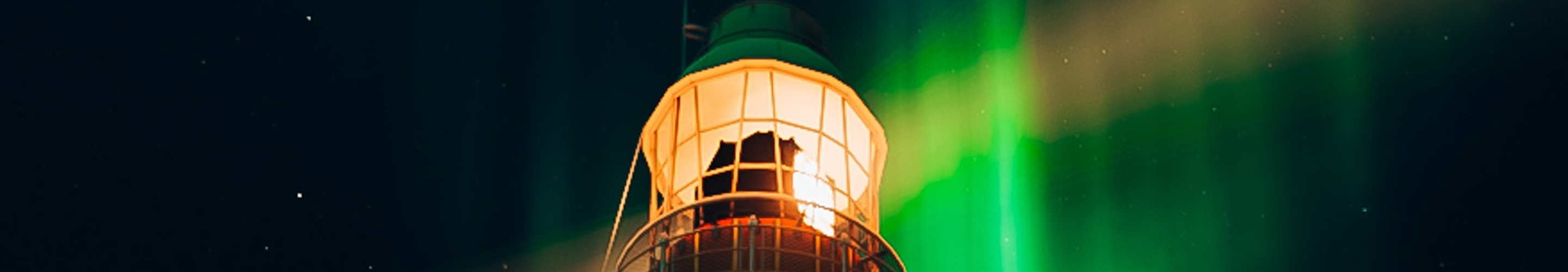 A lighthouse shining in front of green light of the aurora borealis.