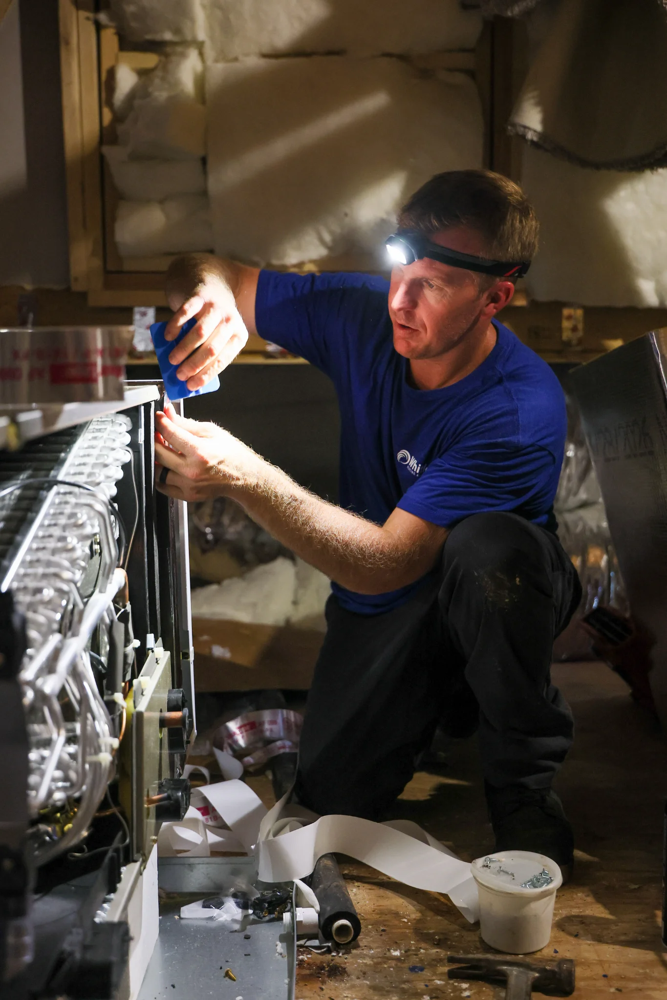 A man wearing a blue t-shirt and black pants, with a headlamp on his forehead, kneels in what appear 