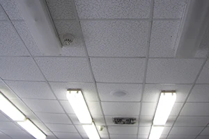 A white drop ceiling with evenly spaced fluorescent light fixtures and a smoke detector. The simple, clean design indicates an indoor commercial or office space.