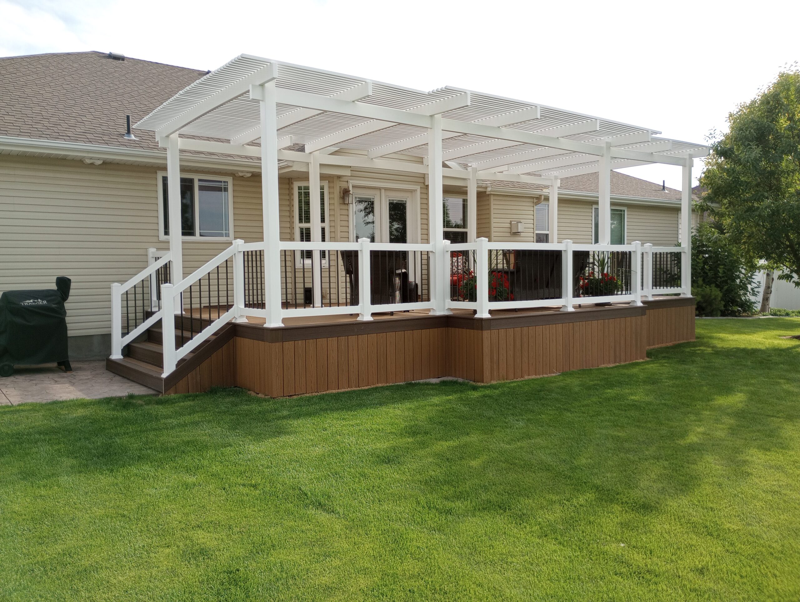 Create a stunning and functional backyard oasis with a custom composite deck and pergola from DeckPro LLC. This project features durable brown composite decking and skirting, perfectly complemented by a large white vinyl pergola for shade. The design is finished with stylish white railings and black metal balusters, offering a perfect blend of beauty and low-maintenance living.