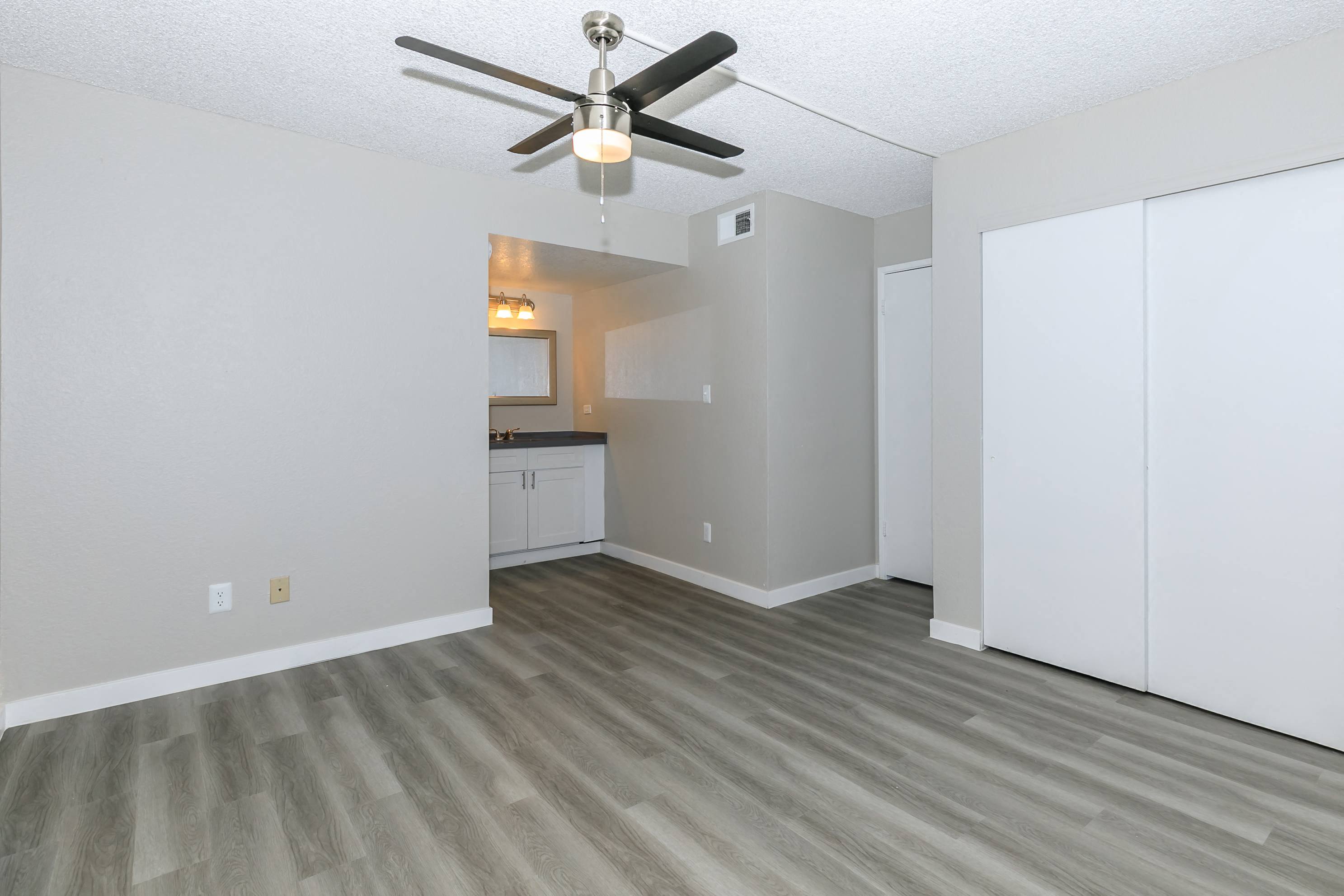 an empty living room with a ceiling fan and a kitchen