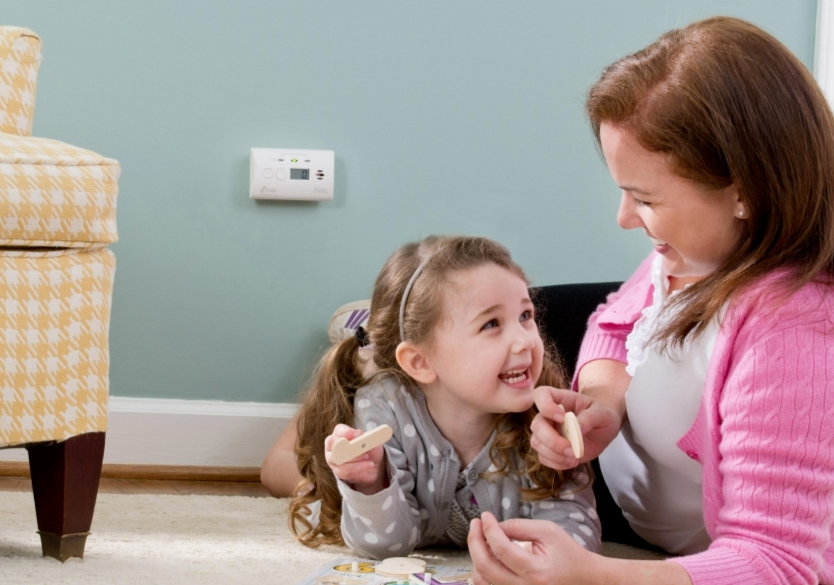 A mom plays with her daughter and a carbon monoxide alarm is plugged in the wall.