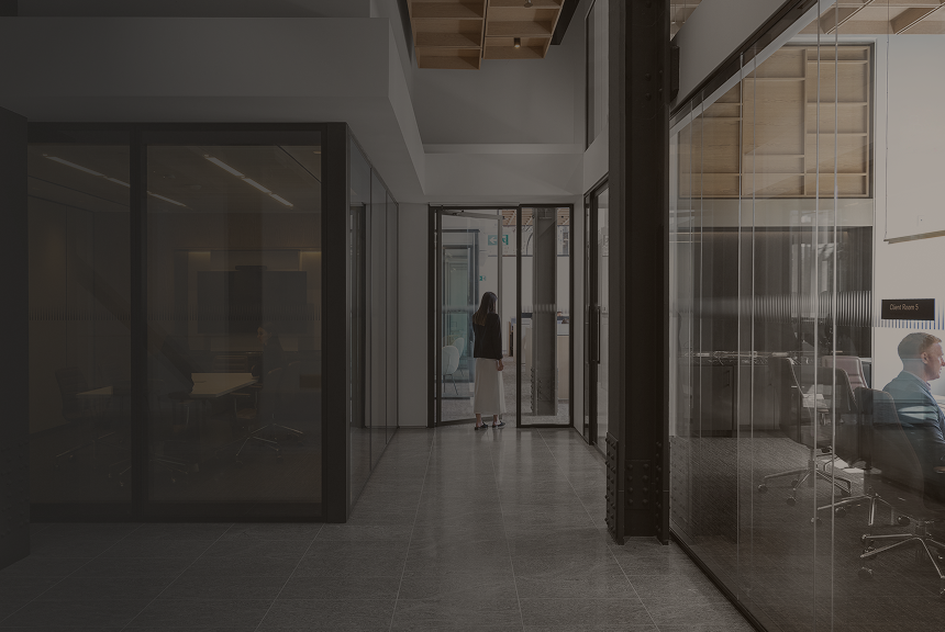 Woman walking down a hallway with glass-walled boardrooms on either side.
