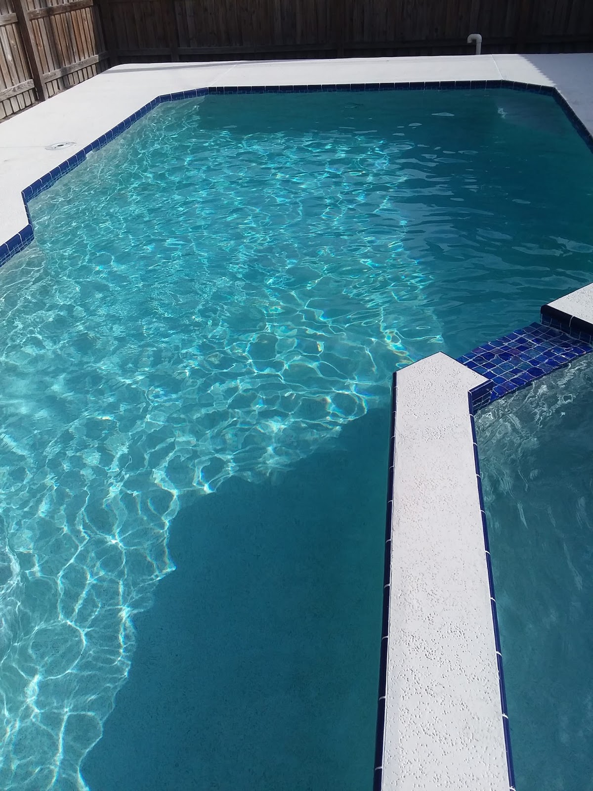 Residential backyard swimming pool with bright turquoise water, geometric edges, and light-colored coping.