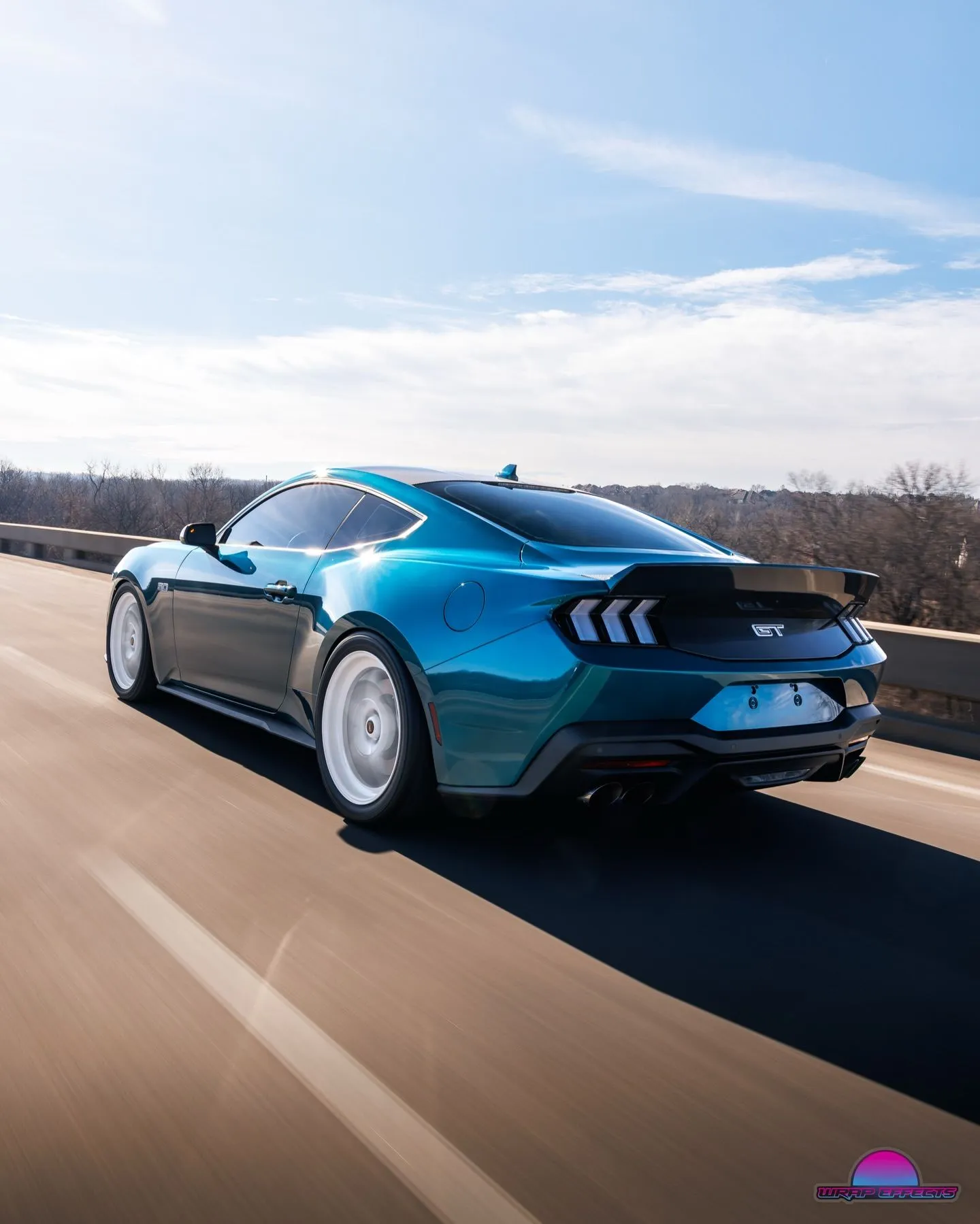 Metallic blue Ford Mustang GT cruising on highway featuring sleek body lines, tinted windows, performance wheels, and custom styling captured in dynamic rolling automotive photography with motion.