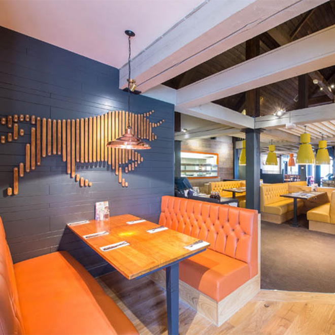 Inside a Whitbread restaurant, in the foreground an orange booth sits underneath a decorative line art piece of a bull.