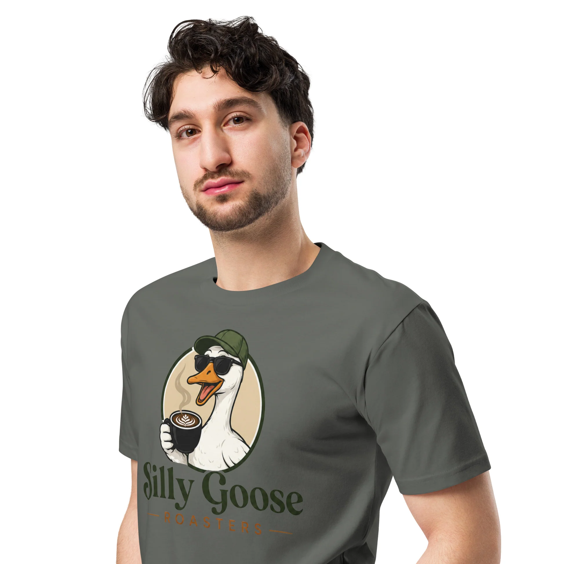 A man wearing a dark grey t-shirt with a graphic of a goose holding a coffee cup and the text "Silly Goose Roasters". The goose is wearing sunglasses and a green baseball cap, and there is latte art on the coffee. The man is looking towards the camera with a neutral expression.
