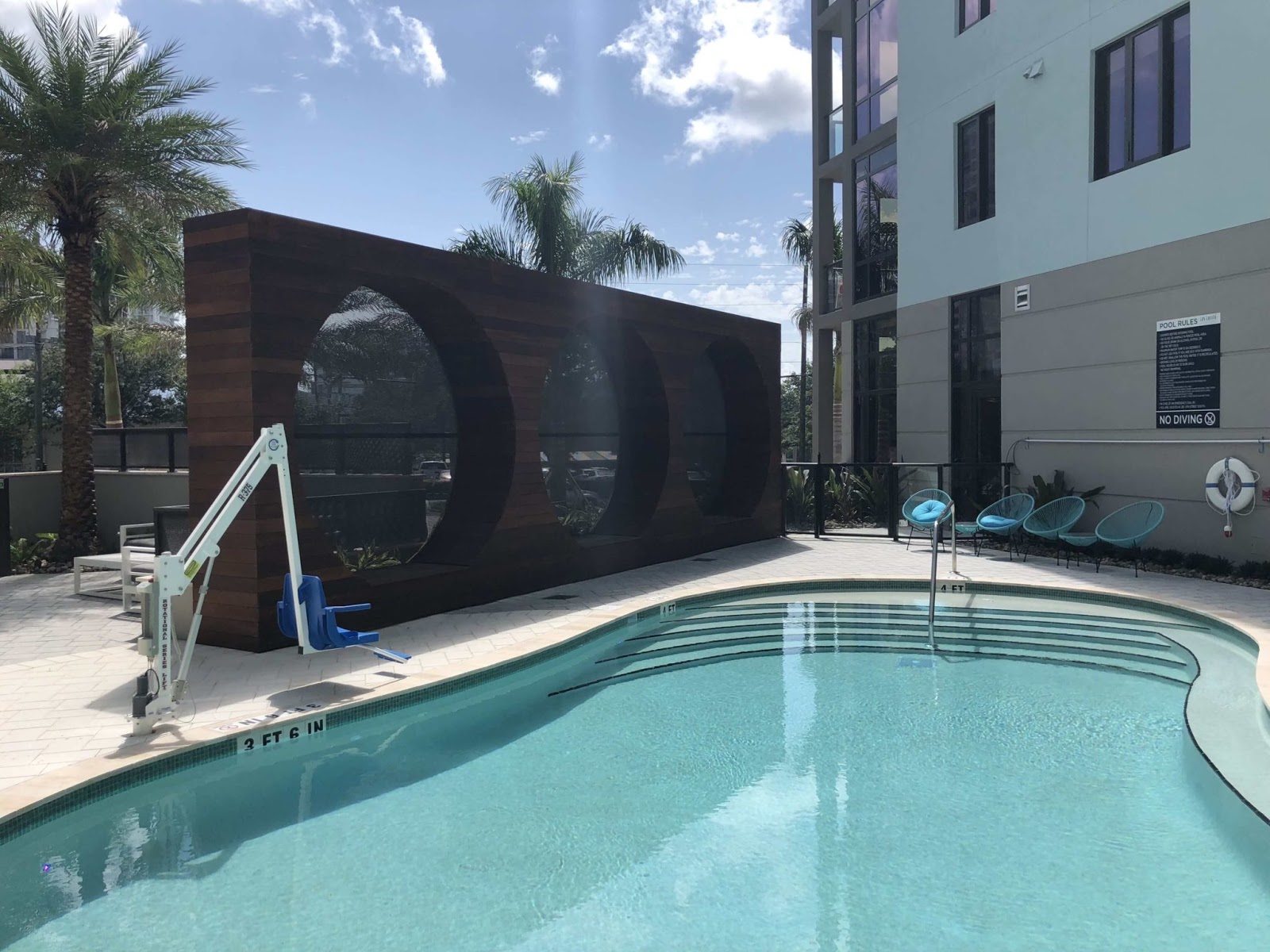 Resort-style backyard swimming pool with deep blue water, set against tall palm trees, clear blue skies, and a modern two-story home.
