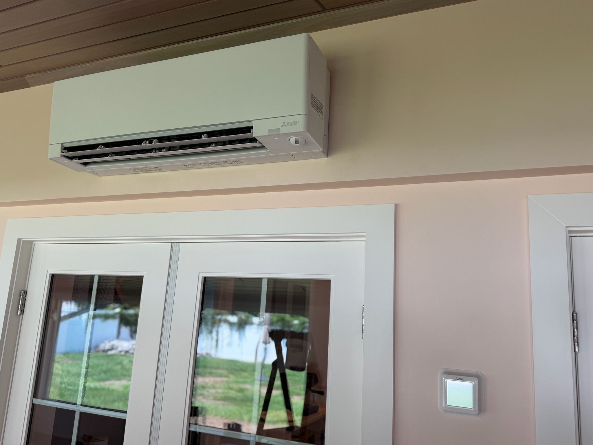 Wall-mounted Mitsubishi ductless mini-split indoor unit installed above double doors, with a nearby  
