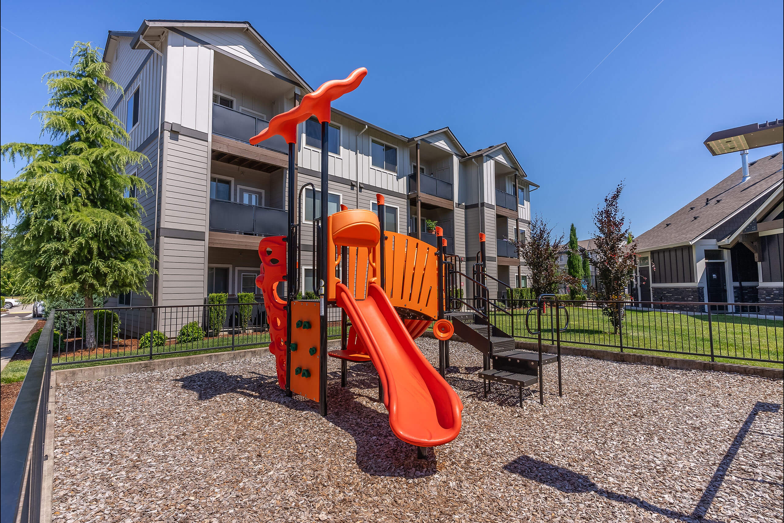 A playground with a slide and a climbing frame in front of a residential building.
