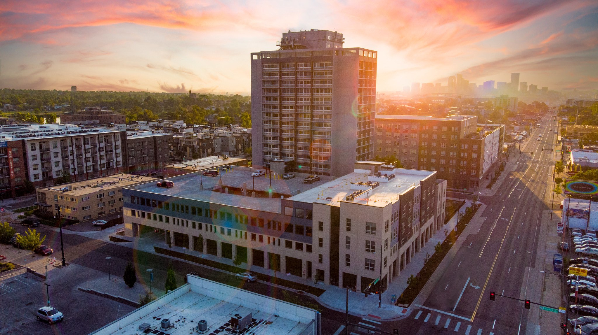 A cityscape with a large building in the foreground and a sunset in the background.