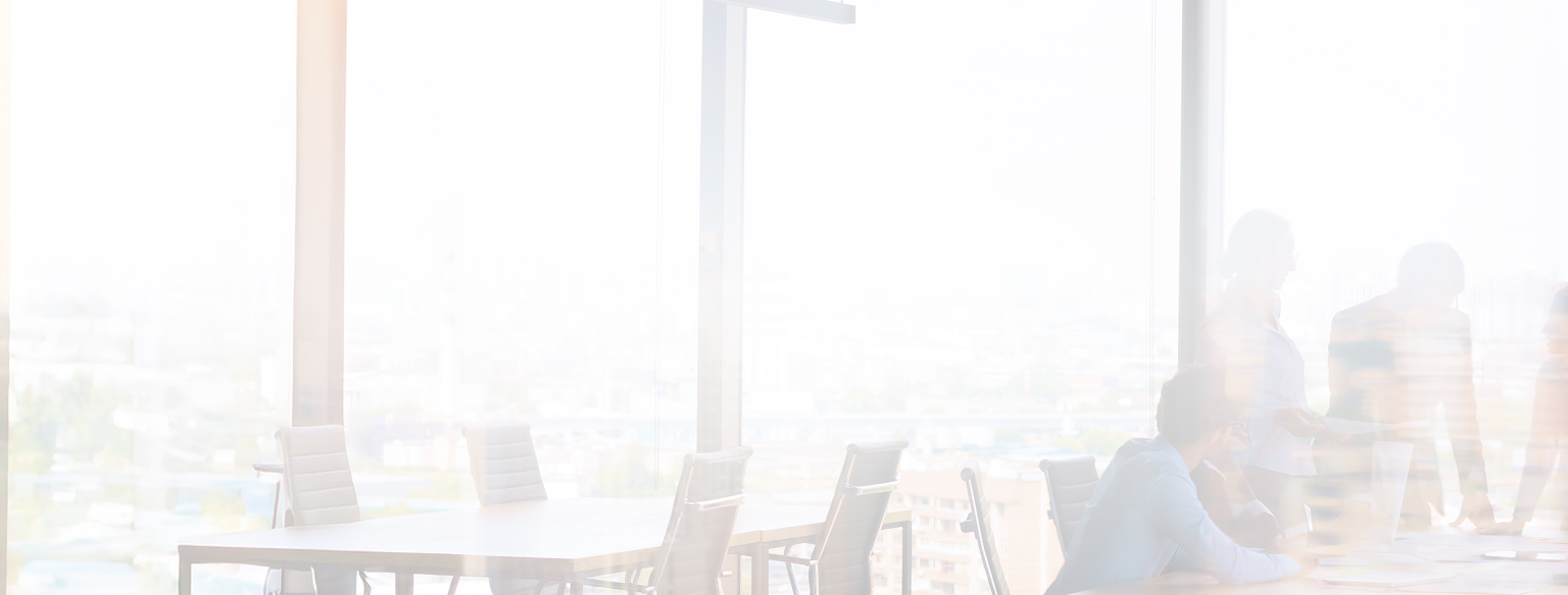 Blurred figures in an a well-lit office meeting room with large windows.