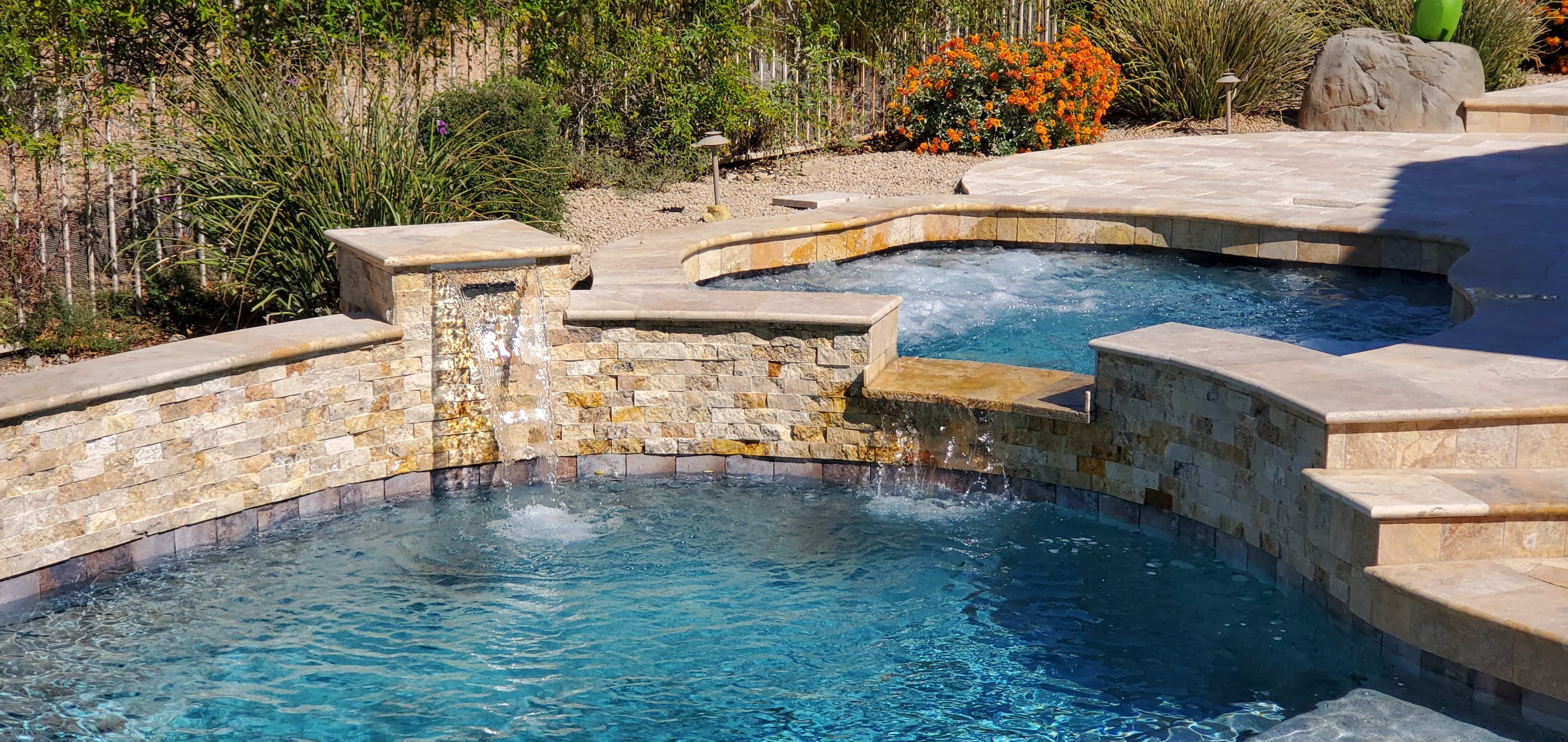 This stunning pool showcases magnificent travertine tile and pool decking, creating a seamless and sophisticated look. Custom spillways from the jacuzzi add a touch of elegance, enhancing both the aesthetic and soothing ambiance of this luxurious outdoor space.