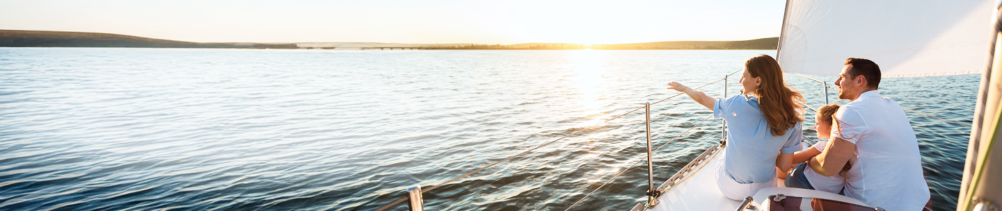 Young parents with their child on the bow of a sailboat enjoying the view.