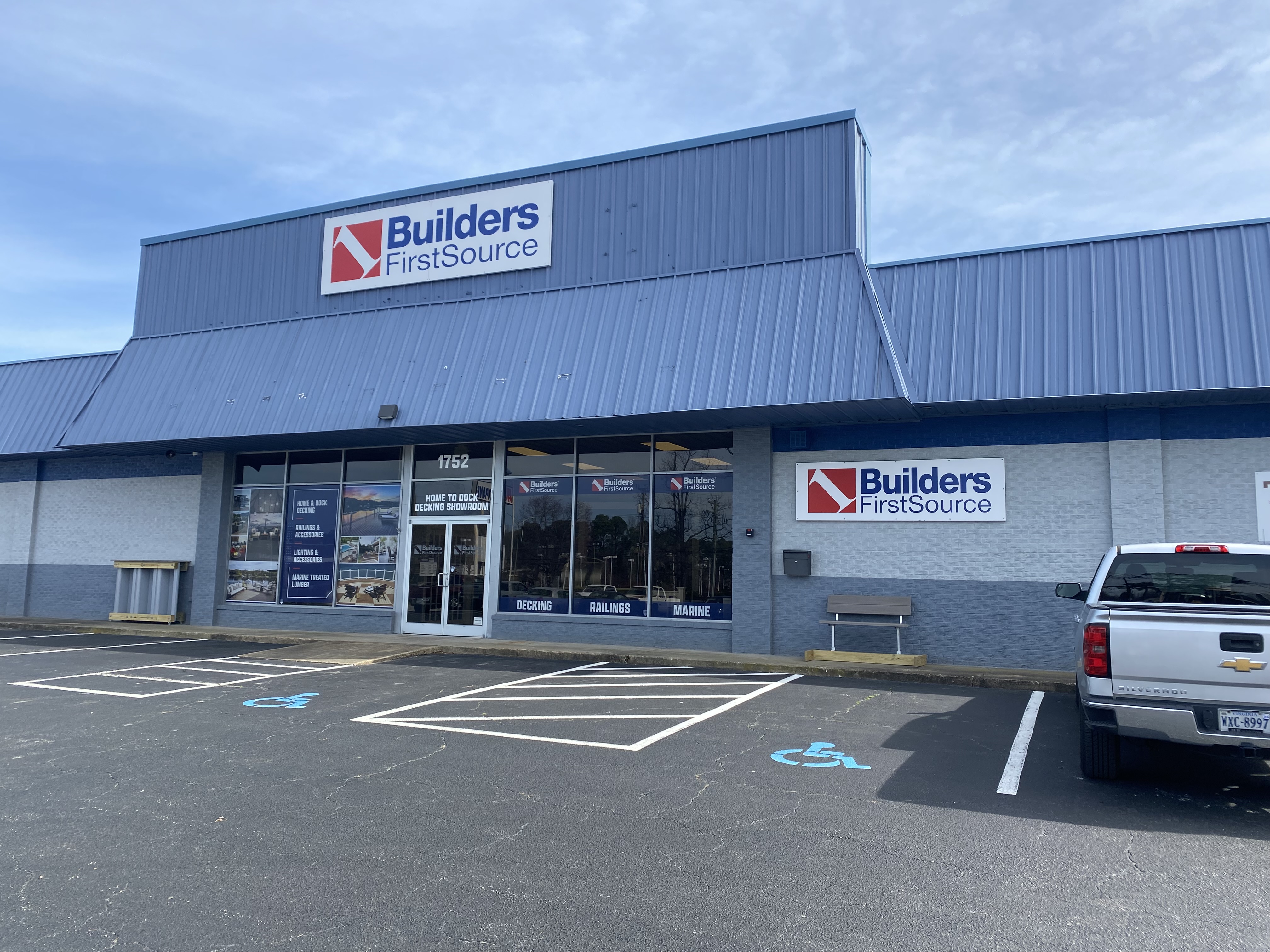 The front entrance of the Builders FirstSource Chesapeake location, specializing in decking, millwork, and building materials. The storefront features large signage, product displays, and accessibility parking, welcoming contractors and homeowners for all their construction supply needs.