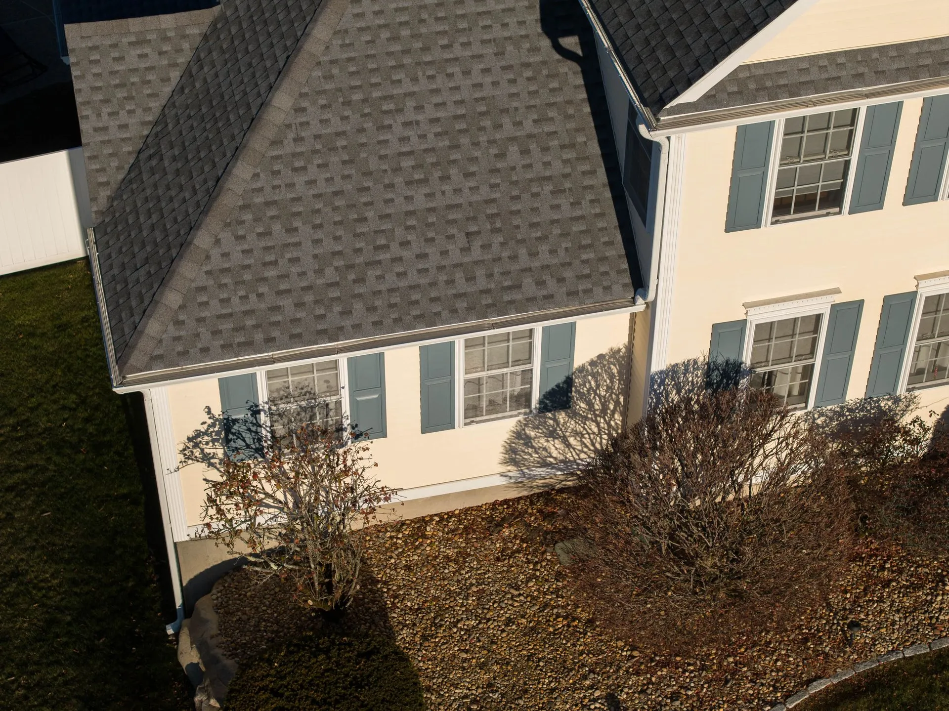 Drone view of a residential property highlighting rooflines, gutters, siding, and landscaping. Profe 