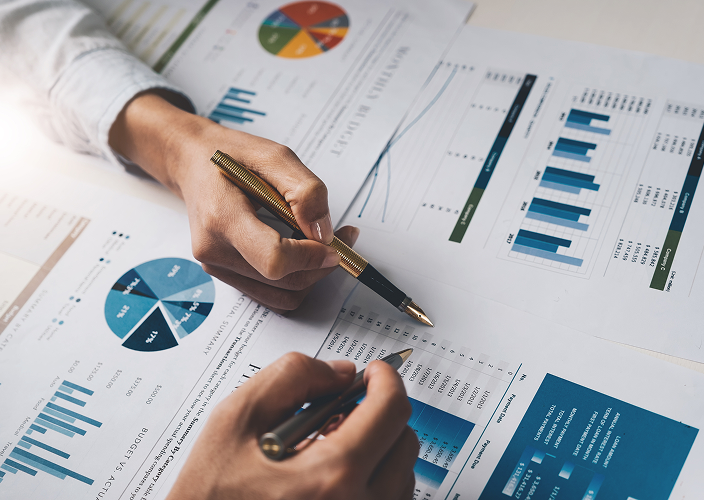 Two people reviewing printed spreadsheets and graphs spread out on a desk.