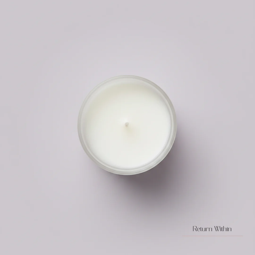 A top-down view of an unlit, white candle in a clear glass jar, resting on a soft grey surface. The candle wax is smooth and creamy, with a small wick centered in the middle. The jar has a frosted appearance around its rim. In the lower right corner, the text 'Return Within' is subtly displayed in a delicate, serif font, accompanied by a thin pink line.