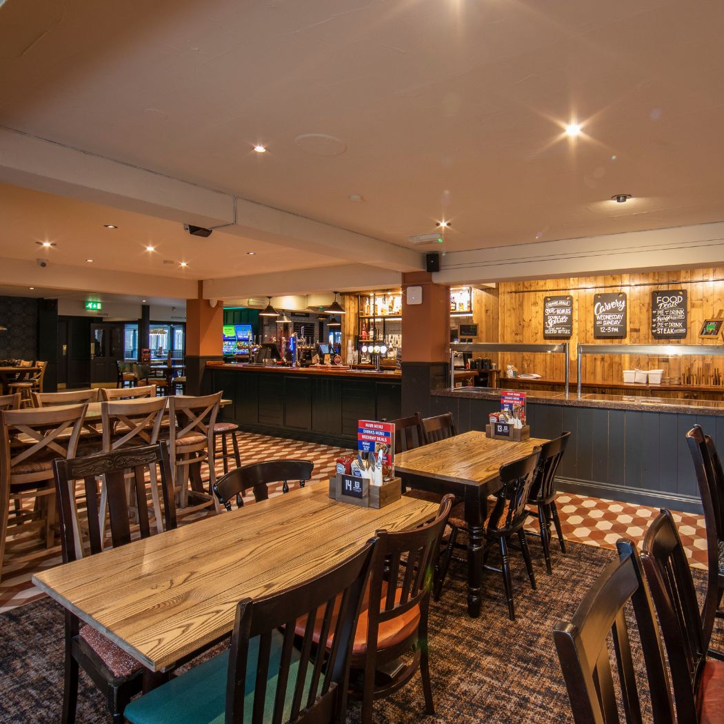 Open bar and dining space inside The Arrow featuring wooden tables, seating and a stocked bar, creating a relaxed setting for meals and drinks.