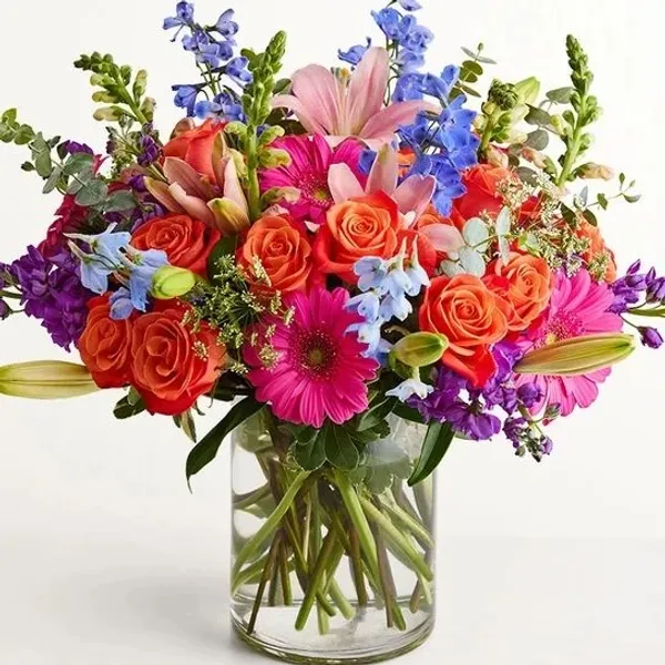 A vibrant bouquet of assorted flowers, including orange roses, pink gerbera daisies, blue delphinium 
