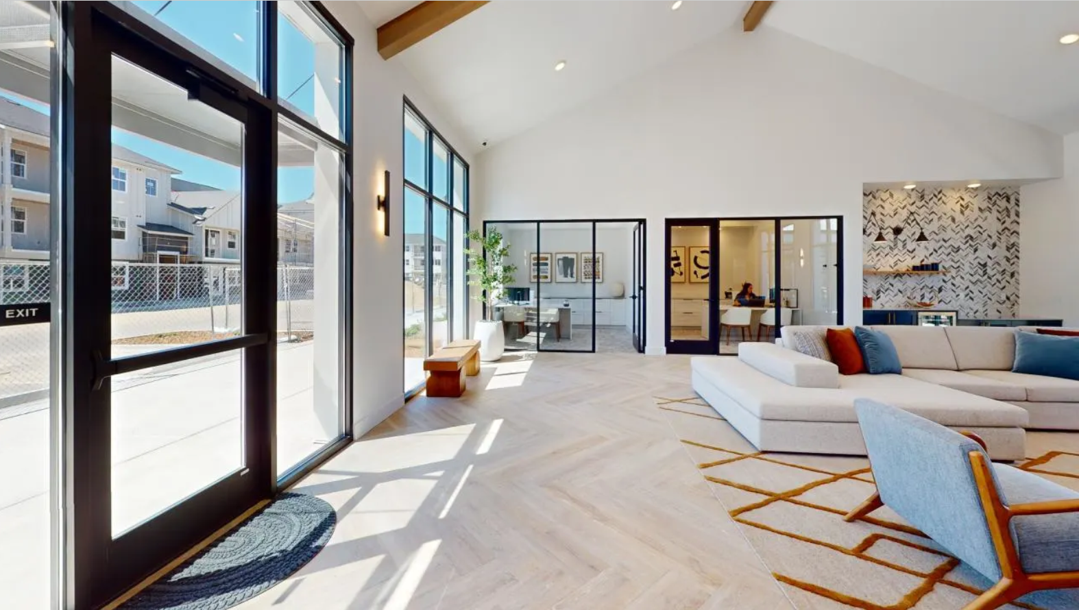 The oversized resident lounge with a cream couch, herringbone pattern plank flooring, oversized windows, and a large glass door