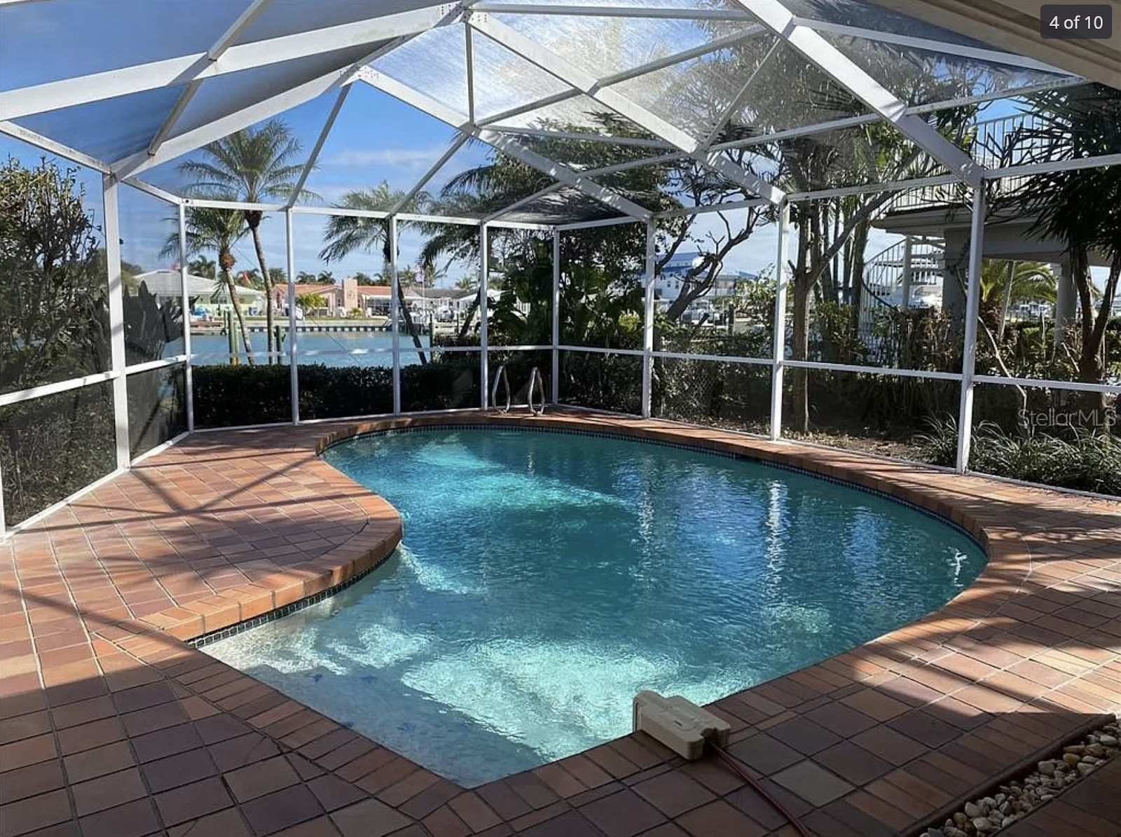 Screen-enclosed backyard swimming pool with clear blue water, brick paver decking, and a private tropical setting.