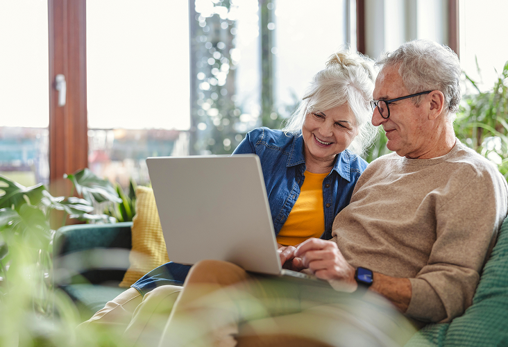 An elderly couple sitting on the couch looking at their laptop.