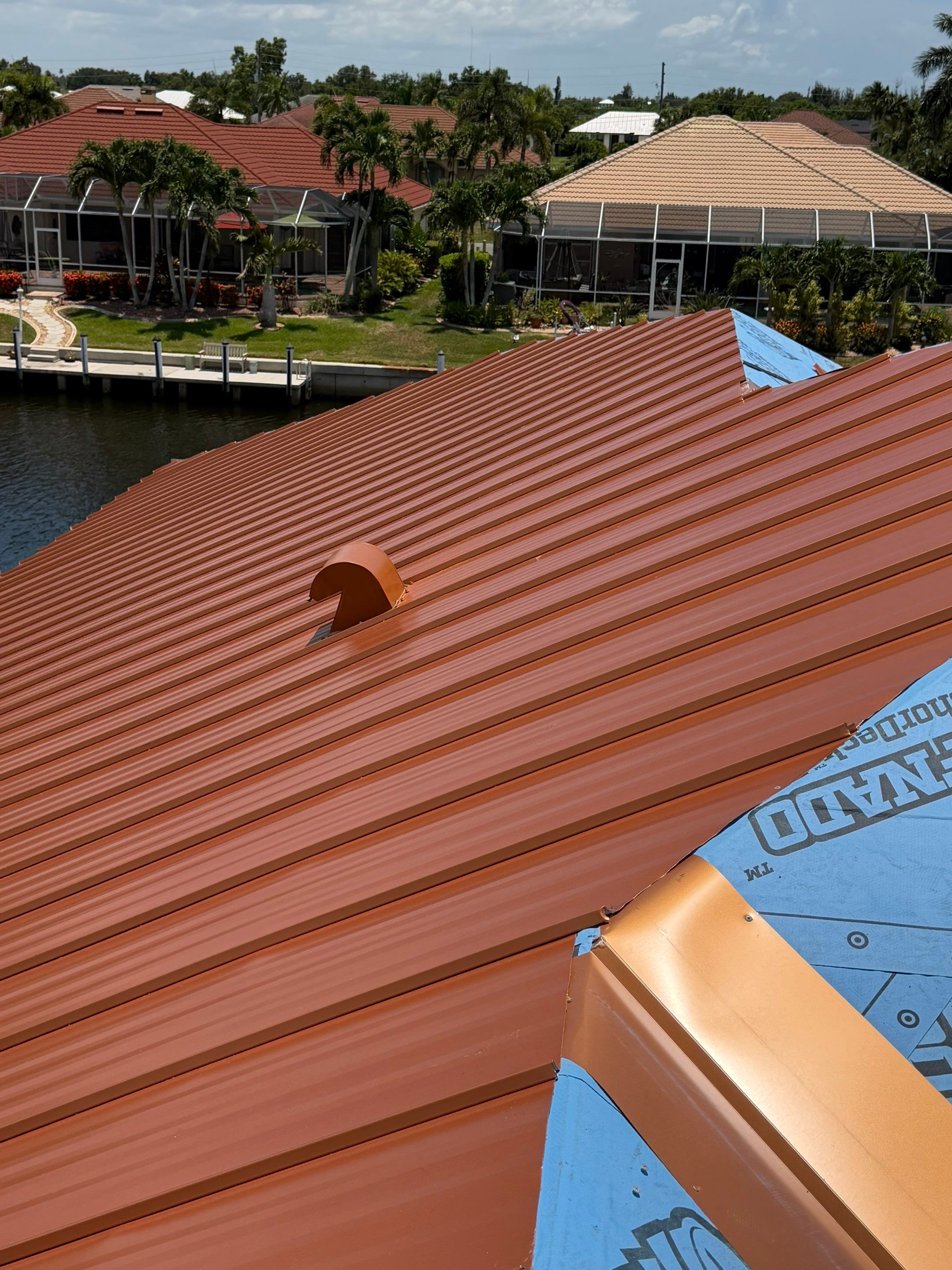 Close-up of roofers securing copper-colored metal roofing panels around a roof valley and entryway s 