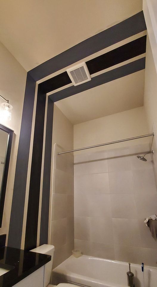 Modern bathroom featuring bold black geometric accent stripes framing the shower, contrasting with white walls, sleek fixtures, tiled surround, and clean finishes that create a contemporary, eye-catching interior design.