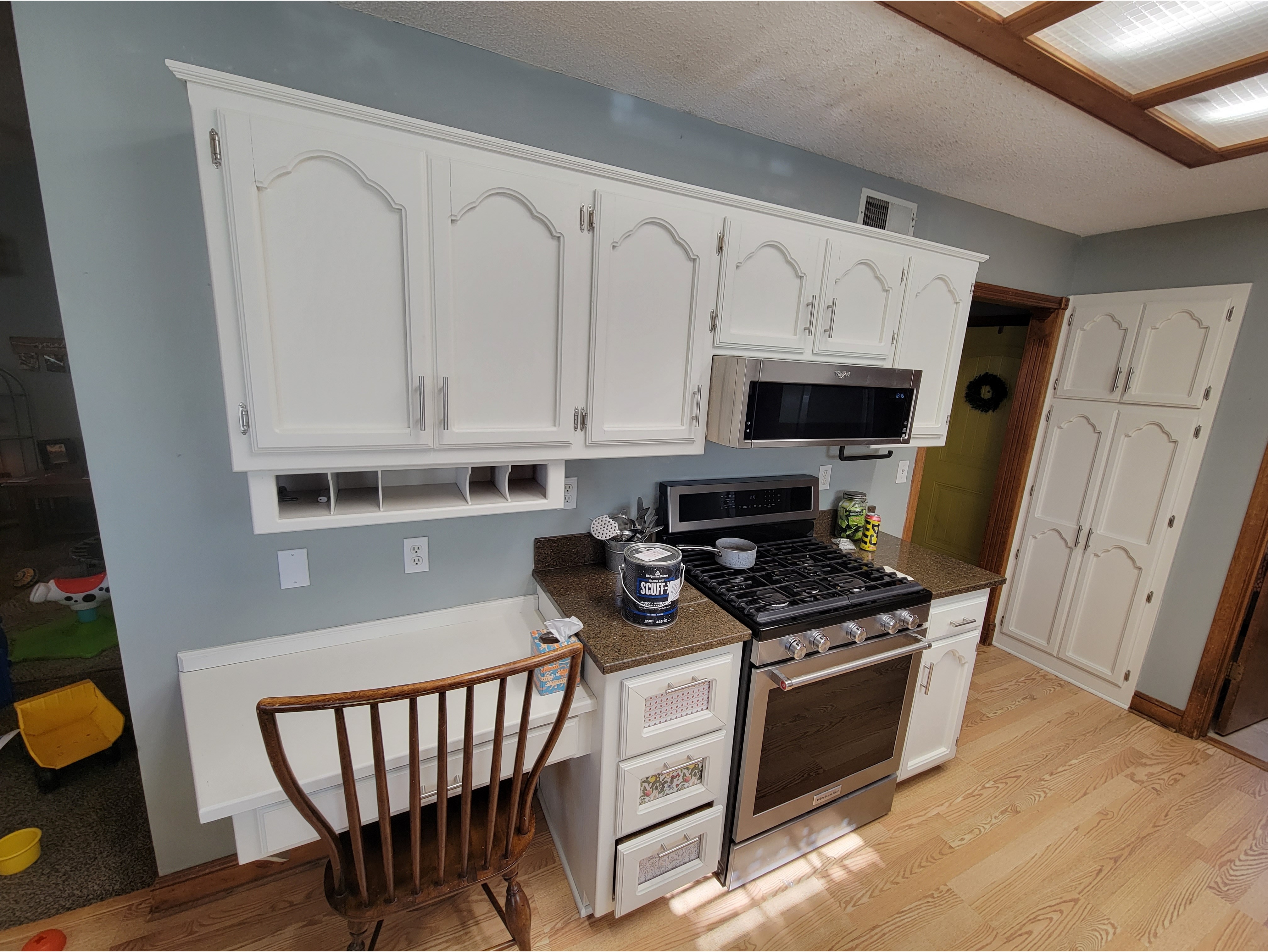 A modern-ish kitchen featuring freshly painted white cabinets with decorative trim and a smooth, updated finish. The space includes a built-in desk area, granite countertops, and stainless steel appliances, highlighting a clean and refreshed design. Ideal for showcasing kitchen cabinet painting and refinishing services for a bright, modern look.