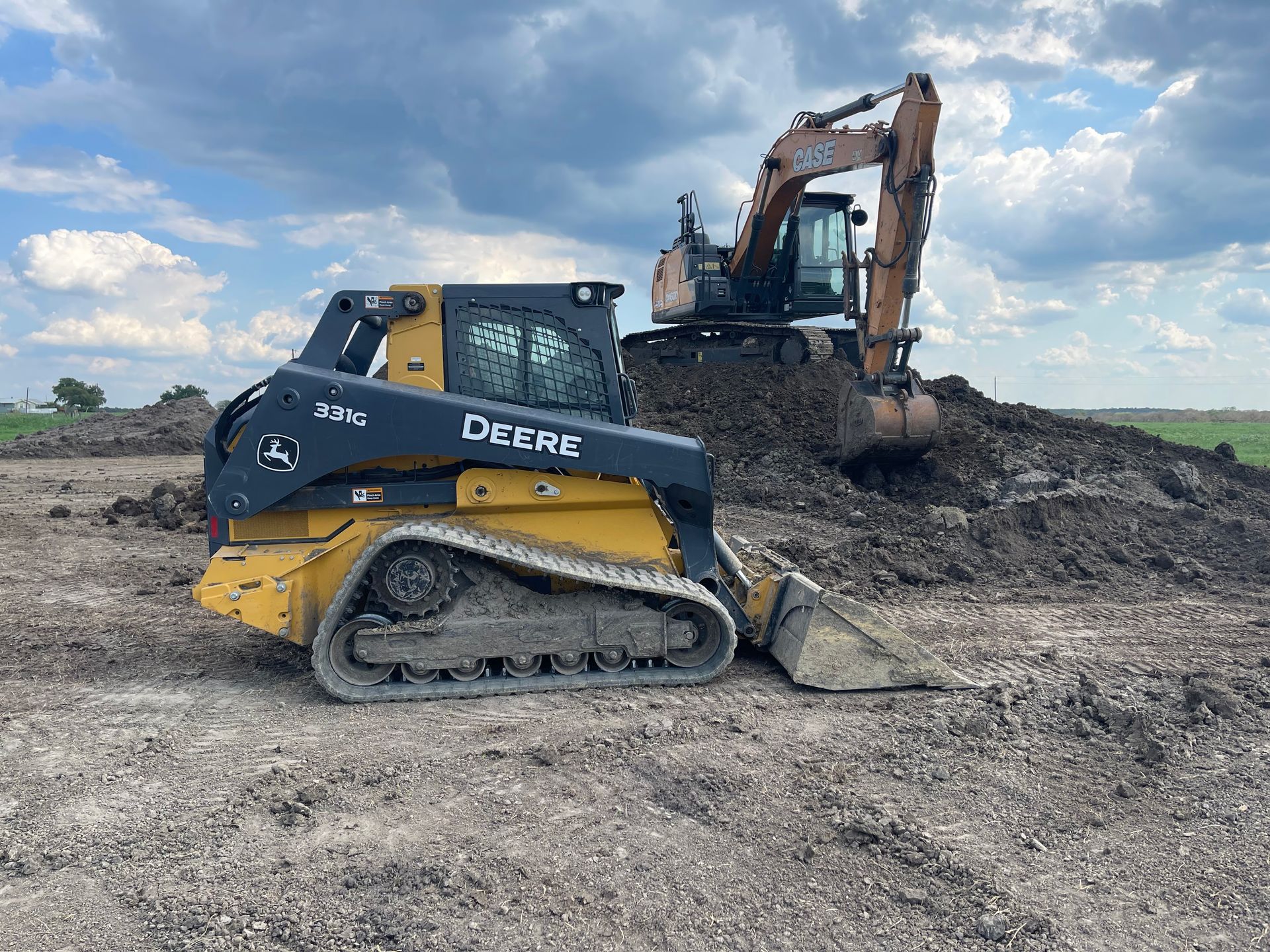 Skid steer loader and excavator working together to move soil and shape terrain on an open construction site, demonstrating efficient excavation, grading, and heavy equipment operation for land development projects.