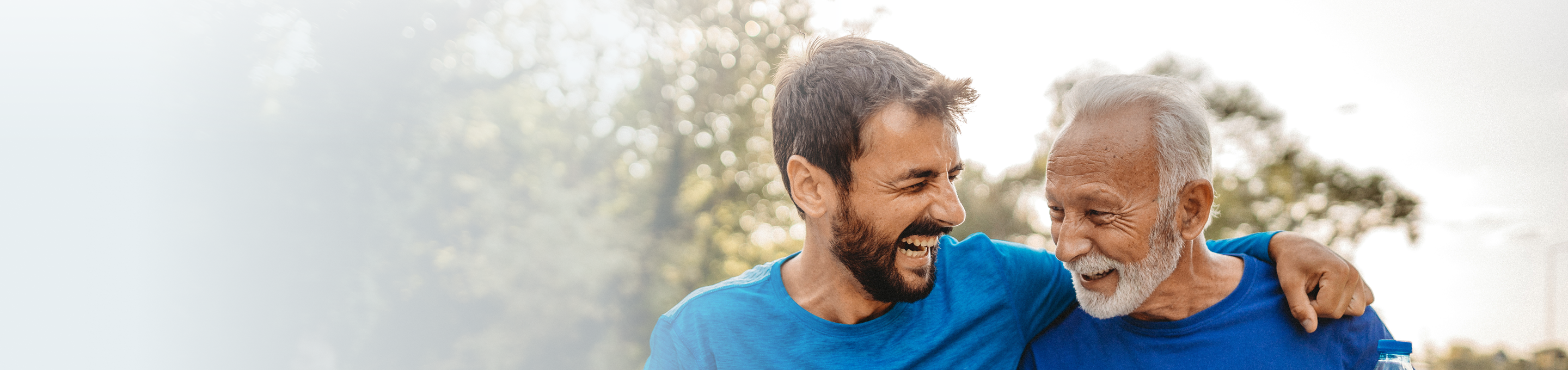 A son laughing alongside his elderly father while they exercise together.