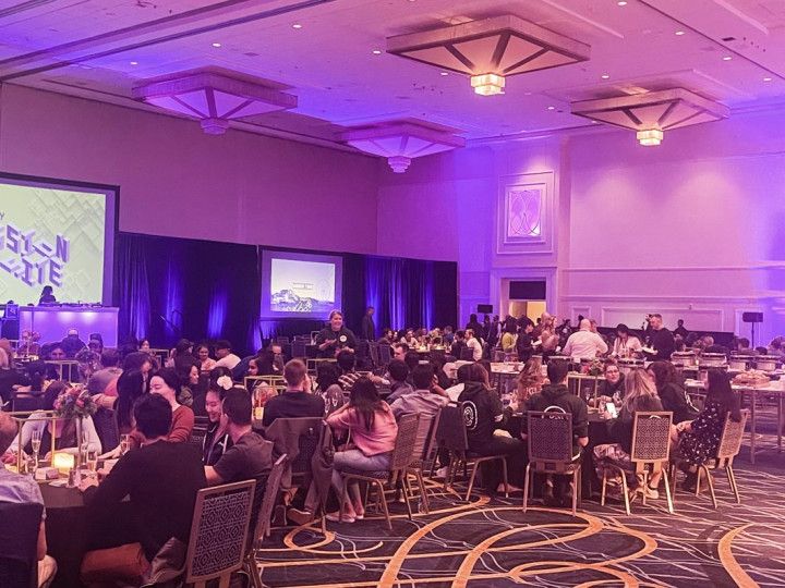 A grand banquet hall filled with people enjoying an event. "MISSION OFFSITE" displayed on the screen, with a DJ playing music.