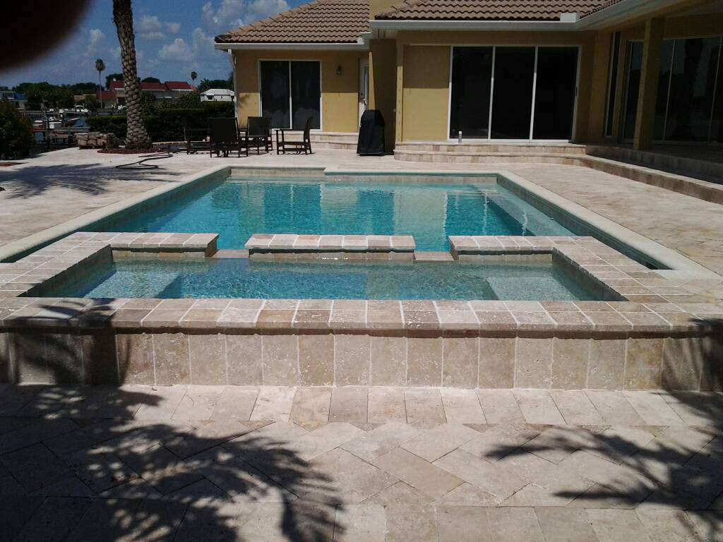 Residential swimming pool with an attached raised spa, light stone decking, and a spacious backyard patio.