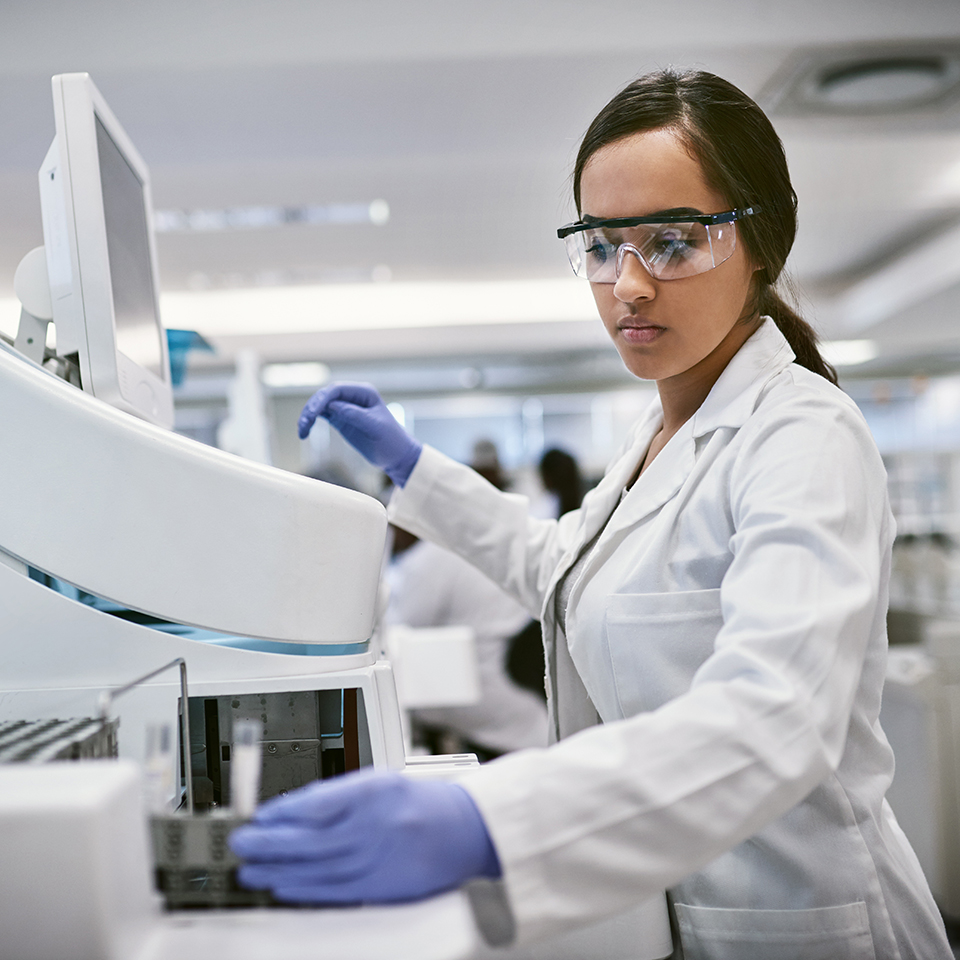 A woman in a white lab coat working with a machine.