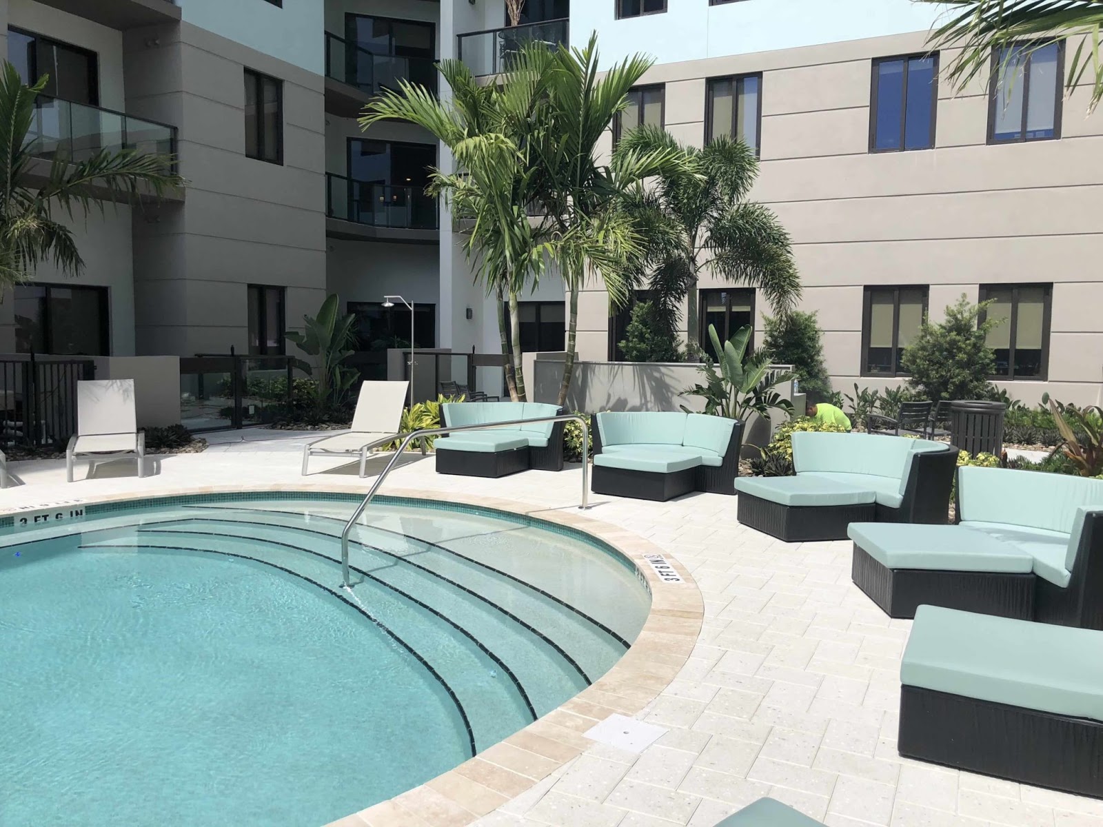 Custom in-ground pool featuring shallow entry steps, wide tan paver patio flooring, and manicured lawn space adjacent to the home exterior.