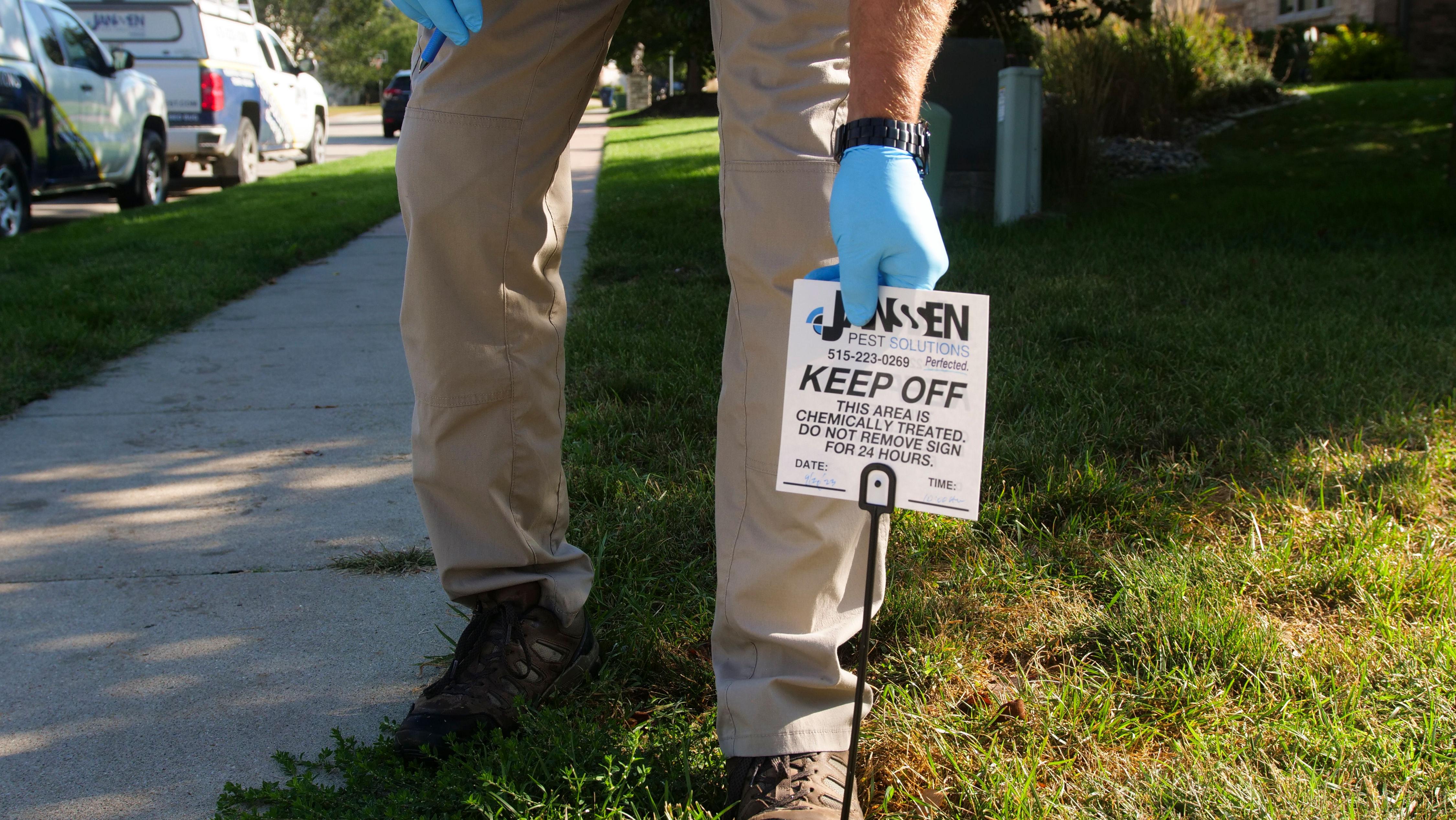 Janssen Pest Solutions technician installing a warning sign to Keep Off this area after pest treatment.