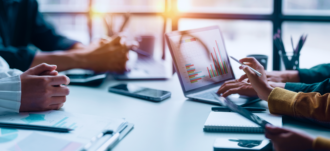 Close-up of people in a meeting pointing at graphs on a laptop screen.