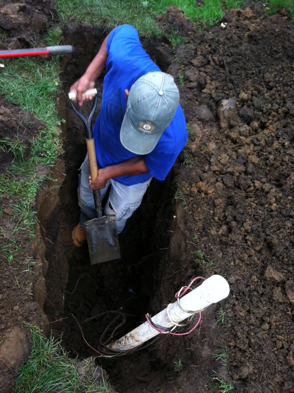 An irrigation technician working inside a dug trench to install or repair underground water pipes for a sprinkler system.