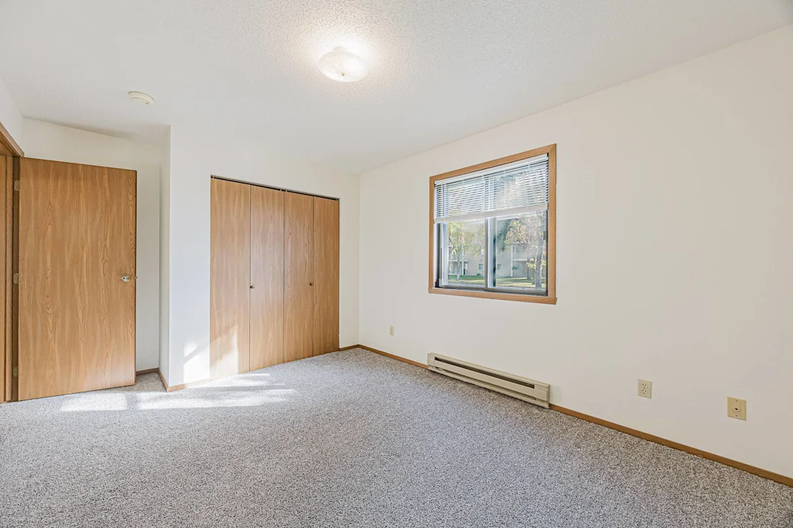 A room with a window, carpet, and two doors, Pine Pointe Apartments, Fargo.