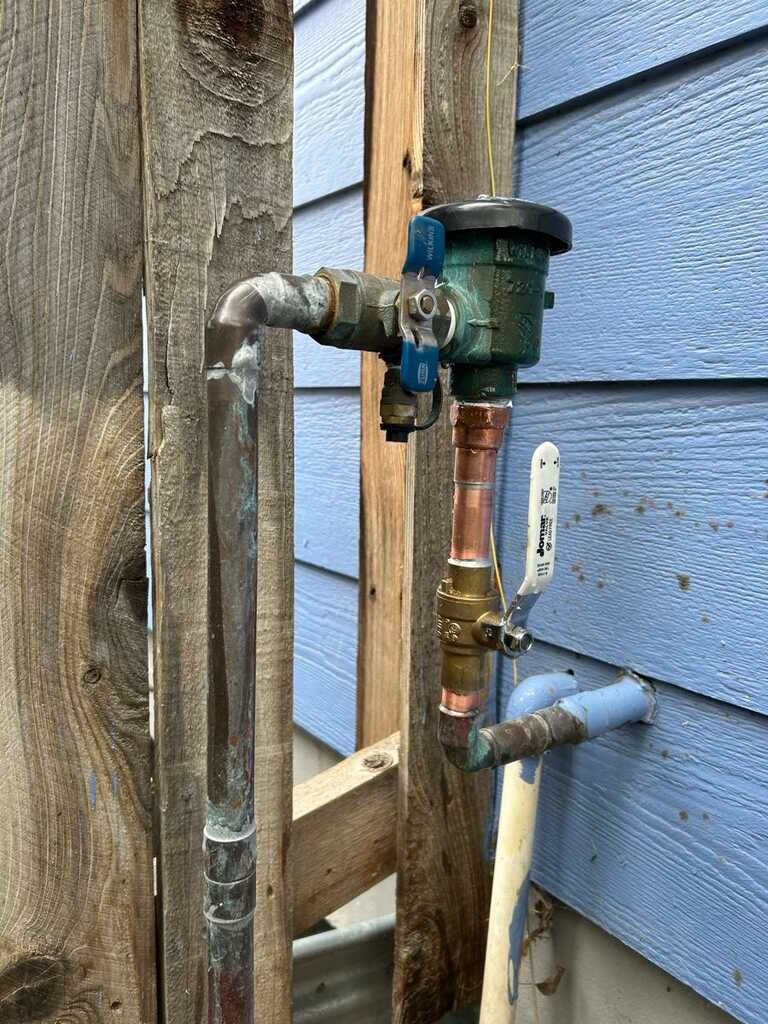 Outdoor plumbing assembly includes galvanized and copper pipes, shutoff valves, and a backflow preve 