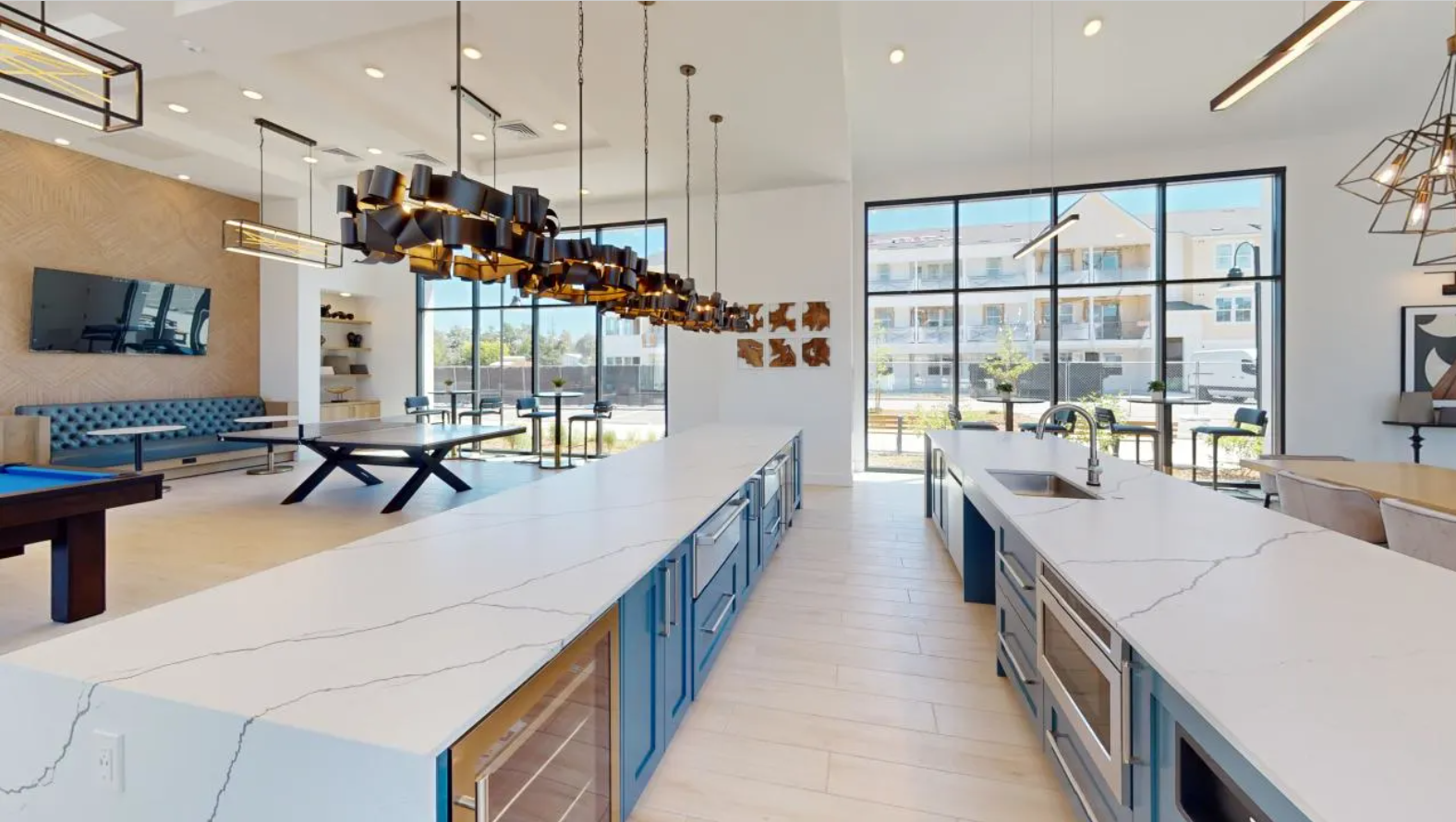 The spacious resident demo kitchen with blue cabinets, sleek appliances, long countertops, and pendant lighting