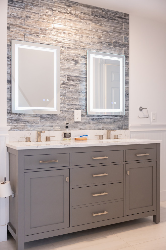 A modern bathroom vanity with two sinks, two backlit mirrors, and gray cabinetry is shown with a textured tile backsplash. A roll of toilet paper is mounted on the left side of the vanity.
