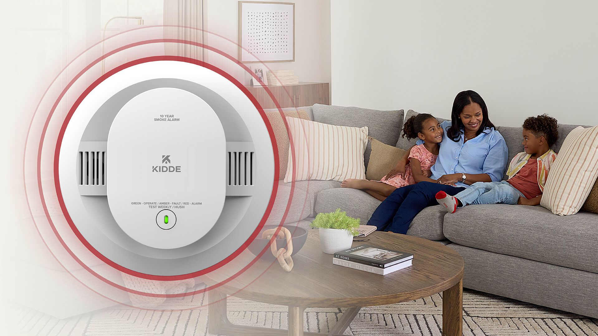 Large smoke alarm in foreground with woman and two kids sitting on couch in background