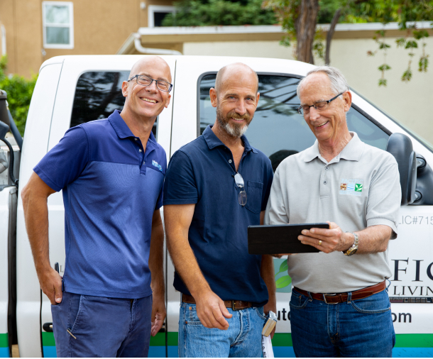 Three smiling men stand beside a branded service van; one holds a tablet as they collaborate outdoors in a friendly, professional setting.